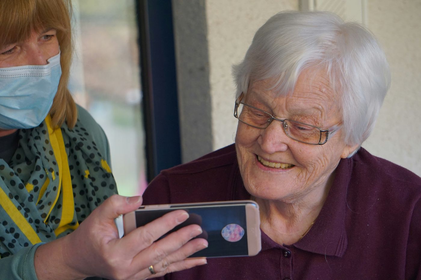 A carer showing an older woman something on a phone.