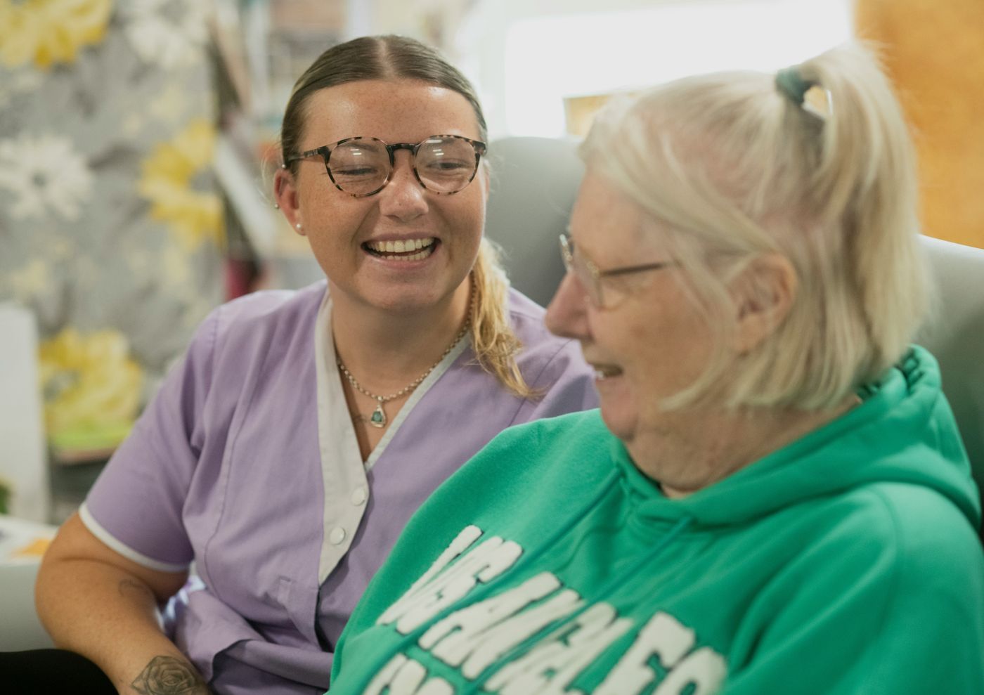A MeddyCare carer laughing with an older woman at home.