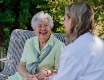 An older woman smiling with her carer in the garden.